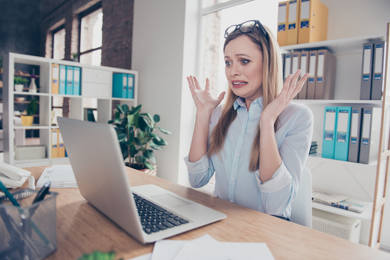 Portrait of charming, emotional, worried, nervous woman with glasses on head and hairstyle gesture with hands, looking at computer, something went wrong, can't get in time, sitting at desk