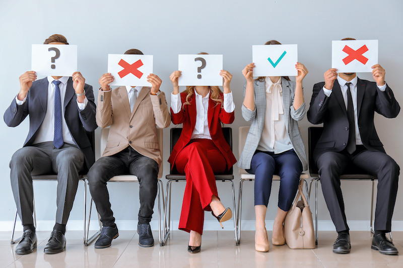 Job applicants holding paper sheets with different marks while sitting on chairs indoors. Job interview concept